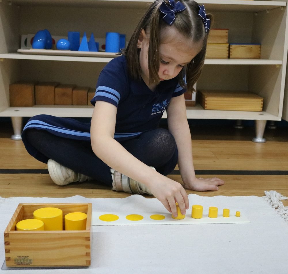 Criança trabalhando com material Montessori de cilindros